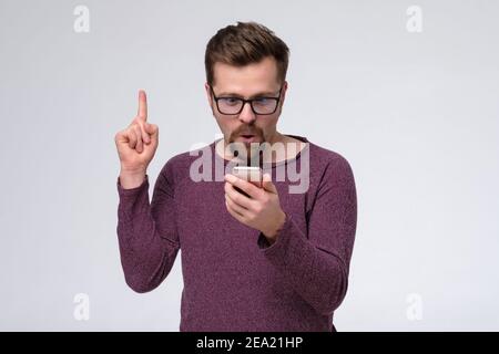 Kaukasischer Mann mit Smartphone zeigt nach oben geben Beratung. Millennial guy sozialen Netzwerk Benutzer halten Handy. Stockfoto
