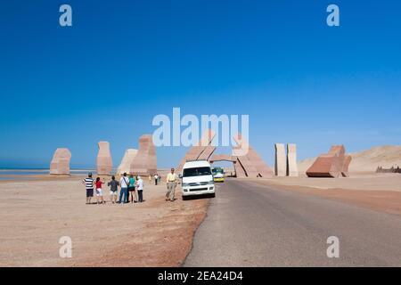 Steinblöcke "Tor von Allah" in Ägypten auf dem Hintergrund des blauen Himmels im Sommer. Im Vordergrund die Straße, Wüste, Menschen, Touristen und Busse Stockfoto