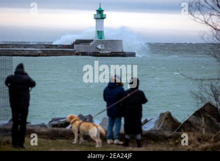 Sassnitz, Deutschland. Februar 2021, 07th. Spaziergänger beobachten beim teilvereisten Leuchtturm am Hafen, wie eine Welle bricht. Starke Winde verursachen Schneewehen und Eisbildung an der Küste im Norden der Insel. Der Deutsche Wetterdienst (DWD) erwartet am Wochenende Schneestürme und Permafrost für Norddeutschland. Quelle: Jens BŸttner/dpa-Zentralbild/dpa/Alamy Live News Stockfoto