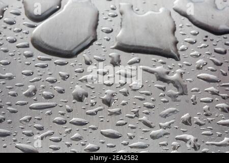 Fototextur Tropfen Wasser auf einem zerkratzten Metallstahl. Makro viele Tropfen Wasser verschiedener Größen auf einem grauen Hintergrund. Große Tropfen auf den ph-wert Stockfoto