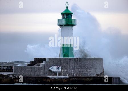 Sassnitz, Deutschland. Februar 2021, 07th. Am teilweise eisigen Leuchtturm am Hafen bricht eine Welle aus. Starke Winde verursachen Schneewehen und Eisbildung an der Küste im Norden der Insel. Der Deutsche Wetterdienst (DWD) erwartet am Wochenende Schneestürme und Permafrost für Norddeutschland. Quelle: Jens BŸttner/dpa-Zentralbild/dpa/Alamy Live News Stockfoto
