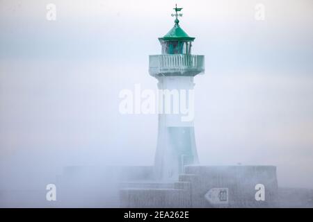 Sassnitz, Deutschland. Februar 2021, 07th. Am teilweise eisigen Leuchtturm am Hafen bricht eine Welle aus. Starke Winde verursachen Schneewehen und Eisbildung an der Küste im Norden der Insel. Der Deutsche Wetterdienst (DWD) erwartet am Wochenende Schneestürme und Permafrost für Norddeutschland. Quelle: Jens BŸttner/dpa-Zentralbild/dpa/Alamy Live News Stockfoto
