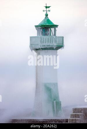 Sassnitz, Deutschland. Februar 2021, 07th. Am teilweise eisigen Leuchtturm am Hafen bricht eine Welle aus. Starke Winde verursachen Schneewehen und Eisbildung an der Küste im Norden der Insel. Der Deutsche Wetterdienst (DWD) erwartet am Wochenende Schneestürme und Permafrost für Norddeutschland. Quelle: Jens BŸttner/dpa-Zentralbild/dpa/Alamy Live News Stockfoto