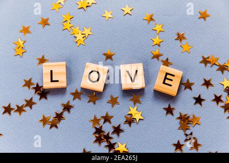 Liebe, bestehend aus Holzwürfeln auf blauem Hintergrund mit goldenen Sternen, Valentinstag. Selektiver Fokus. Stockfoto
