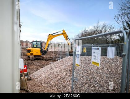 Gelb Bagger Bagger mit Schaufelarm verlängert arbeiten auf moderne Baustelle mit Steinhaufen und neuen Häusern gebaut Im Hintergrund am Sommertag Stockfoto