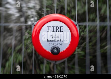 Bright Red Metal Feueralarm Glocke drehen Griff zu bedienen Alarm manuelles Stahlklingeln auf der an angeschlossenen Baustelle Metallzaun Stockfoto