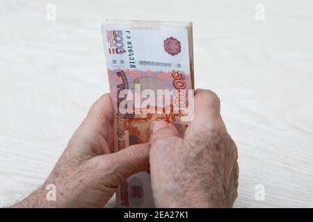 Hände einer älteren Frau Nahaufnahme mit einem Bündel von russischem Geld in 5000 Rubel. Hände liegen auf dem Tisch und Banknoten liegen vertikal in t Stockfoto