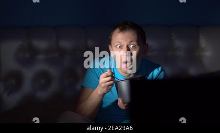 Mann schaut nachts Fernsehen und isst Eis. Überraschendes Gesicht. Bewegte Kamera Stockfoto
