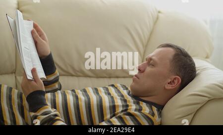 Porträt eines jungen Mannes. Auf der Couch liegend, ein Buch lesend Stockfoto