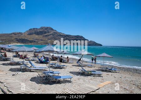 Plakias Strand ist in Kreta, Griechenland: Plakias Strand an der Südküste der griechischen Insel Kreta. Blaue Sonnenschirme und Bettsteine am Strand. Stockfoto