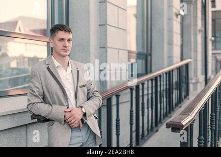 Ein angehende junge Mann in formeller Kleidung posiert auf der Veranda eines Bürogebäudes in der Stadt Stockfoto