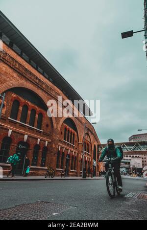 London UK Januar 2021 Vertikale Weitwinkelaufnahme eines Radfahrers, der an einer Londoner Straße vorbeifährt, Bahnhofsbereich. Dramatische launische Winteraufnahme Stockfoto