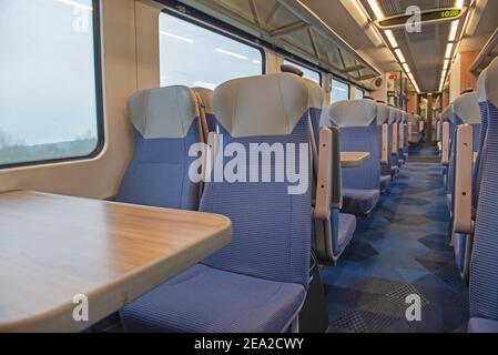 Blick auf das Innere in einem menschenleeren Pendlerzug Wagen Mit Sitzreihen und Tischen Stockfoto