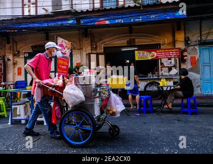 Ein männlicher Straßenhändler schiebt einen Trolley an einem Restaurant im Freien in Chinatown, Bangkok, Thailand vorbei Stockfoto