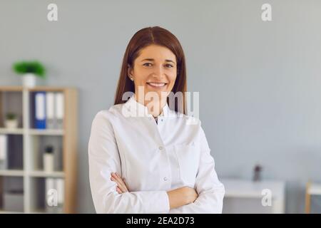 Porträt einer freundlichen Ärztin, die mit gefalteten Armen im Krankenhaus steht und die Kamera anschaut. Stockfoto