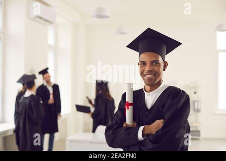Porträt eines lächelnden afroamerikanischen Absolventen, der mit einem Diplom steht und die Kamera anschaut. Stockfoto