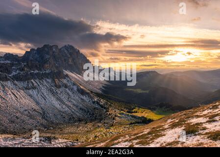 Die verschneiten Geisler-Gipfel in den Puez-Geisler Bergen gegen die Sonne, dramatisch golden erleuchteten Himmel und Wolken bei Sonnenuntergang in den Dolomiten im Herbst, Italien Stockfoto