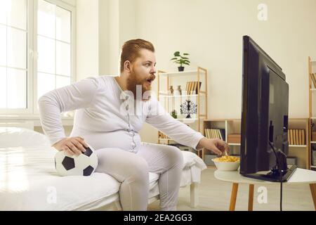 Lustiger Mann beim Fußballspiel im Fernsehen zu Hause und Popcorn essen Stockfoto