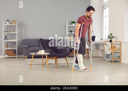 Mann mit gebrochenem Bein versucht, mit Krücken zu gehen Zu Hause und gute Fortschritte zu machen Stockfoto