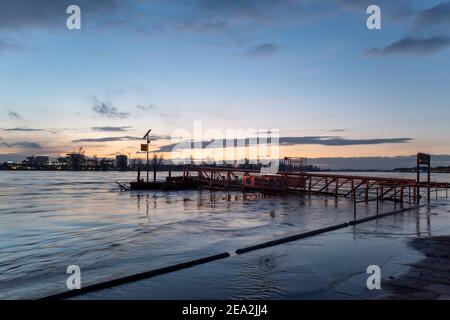 Überschwemmtes Gebiet entlang der Uferpromenade am Rhein und der Hängebrücke am Abend mit wunderschönem Sonnenuntergang und Abenddämmerung. Stockfoto