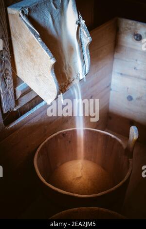 In einem Eimer in der historischen Mühle im Mühlental von Campill, Südtirol, Italien, tropft Mehl aus der Holzmühle Stockfoto