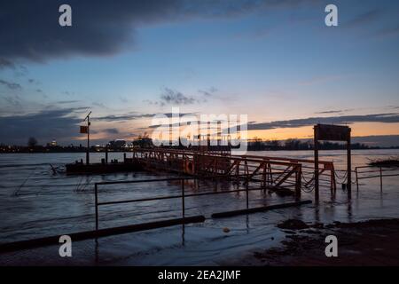 Überschwemmtes Gebiet entlang der Uferpromenade am Rhein und der Hängebrücke am Abend mit wunderschönem Sonnenuntergang und Abenddämmerung. Stockfoto