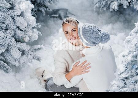 Mann küsst und umarmt seine Frau und Schnee fällt. Liebe zum neuen Jahr. Die Menschen trugen Pelzkopfhörer, Hüte, weiße Pullover. Stockfoto