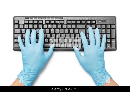 Person arbeitet in medizinischen Schutzhandschuhen und gibt Text auf Die Tastatur eines PCs Stockfoto
