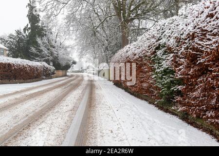 Blick auf eine schneebedeckte, von Bäumen gesäumte Boston Spa High Street mit Spuren, die von Fahrzeugen erstellt wurden, die entlang der Straße fahren Stockfoto