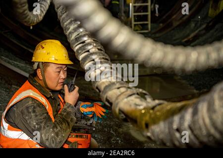 (210207) -- URUMQI, 7. Februar 2021 (Xinhua) -- EIN Arbeiter spricht mit seinem Kollegen durch Walkie-Talkie auf der Baustelle des Tianshan Shengli-Tunnels im Nordwesten Chinas Xinjiang Uygur Autonome Region, 4. Februar 2021. Der Tianshan Shengli-Tunnel ist mit einer Gesamtlänge von rund 22 Kilometern derzeit der längste im Bau befindliche Autobahntunnel in China. Der 2020 begonnene Tunnel, ein sechsjähriges Projekt auf der Urumqi-Yuli-Autobahn, durchläuft eine kalte und hochgelegene Zone mit rauem Klima und geologischem Zustand. Nach der Fertigstellung und für den Verkehr geöffnet, wird es sicherer und mehr conveni Stockfoto