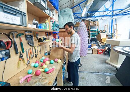 GROSSBRITANNIEN, London, Bombas und Paar, Set-Designer arbeiten in Studio Malerei Kunststoff Früchte. Stockfoto