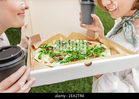 Freundinnen teilen sich eine Pizza zum Mitnehmen. Sie essen leckeres Fastfood und trinken Kaffee und geselligen sich auf einem gemütlichen Stadtplatz Stockfoto