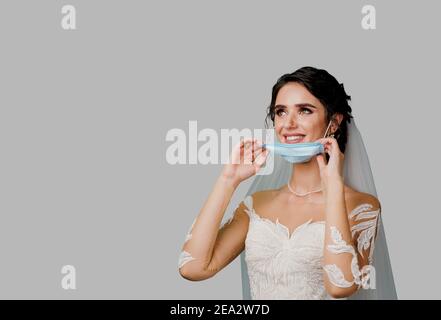 Braut in der medizinischen Maske und Hochzeitsstrauß bei coronavirus covid-19 Quarantänezeit. Attraktive Mädchen nimmt aus Maske und sieht auf der linken Seite mit leeren pla Stockfoto