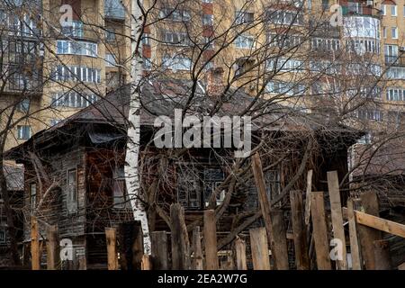 Ein Birkenhaus und ein altes Wohnhaus auf dem Hintergrund eines modernen mehrstöckigen Gebäudes in Perm City, Russland Stockfoto