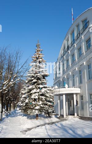 Weihnachtsbaum mit Spielzeug in Form einer natürlichen blauen Fichte im Schnee in der Nähe des Gemeindegebäudes. Zvenigorod / Russland - 2021 01 18: Städtischer Winter Stockfoto