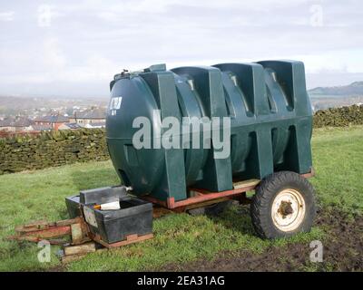 Großer grün geformter Kunststoff-Wassertank auf zwei Rädern Anhänger Auf dem Feld des Bauernhofs Stockfoto