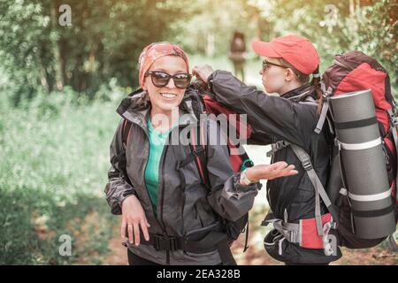 Zwei weibliche Touristen reisen mit Trekkingrucksäcken durch den Wald. Freunde überprüfen sich gegenseitig Ausrüstung und Spaß haben Stockfoto