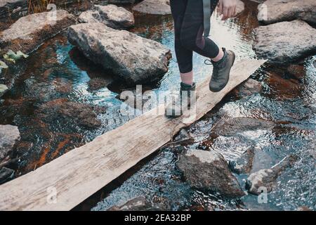 Wanderer Mädchen wades über den Fluss auf einem Holzbrett, schwere Wanderstiefel Stockfoto