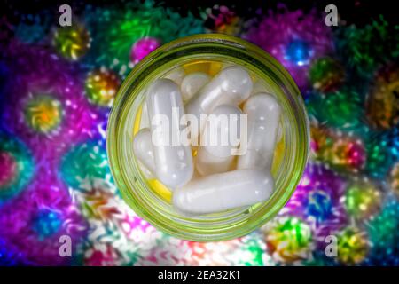 Weiße Pills in gelbem Glasglas auf psychedelischem Hintergrund. Seltsames Buntes Muster. Geistige Reise Reflexion. Stockfoto