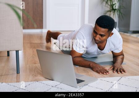 Nahaufnahme eines starken afroamerikanischen Mannes beim Training in horizontaler Plank Position mit Laptop Stockfoto