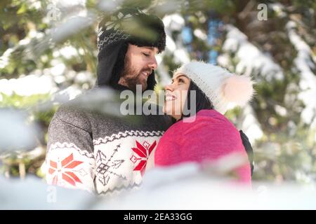 Portrait von fröhlichen Paar, die einander angucken und umarmen Im Winterwald Stockfoto