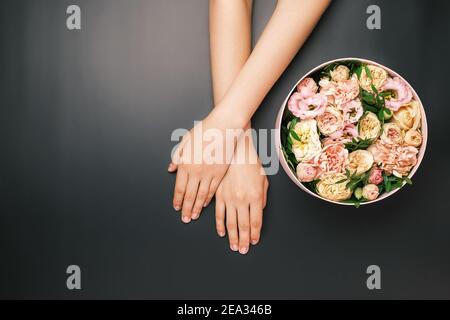 Box mit schönen Blumen neben Womans Hände auf dem schwarzen Hintergrund mit Kopierraum. Beauty salone Card Konzept. Geschenk für 8 März, Muttertag Stockfoto