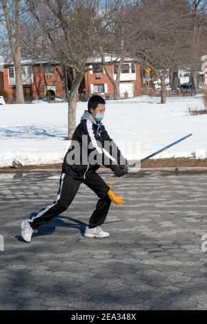 Ein junger chinesischer Amerikaner macht anmutig Tai Chi mit Schwertübungen im Kissena Park in Flushing, Queens, New York City. Stockfoto