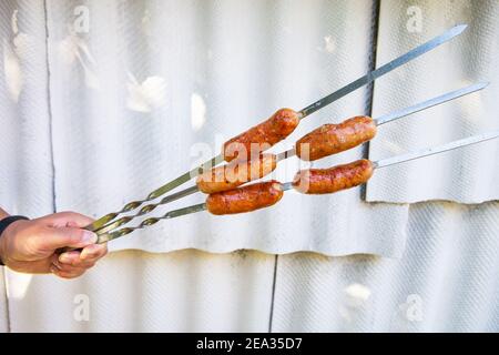 Bayerische Grillwürste, heiße Würste am Spieß. Grill in der Hand unter freiem Himmel auf weißem Hintergrund Stockfoto