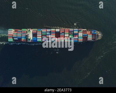 Luftaufnahme von einer Drohne eines Containerschiffes, das Bulk-Container durch eine der belebtesten Schifffahrtsstraßen Asiens transportiert - den Lamma-Kanal - zwischen Aberdeen auf der Insel Hongkong und Lamma. Die Route ist so stark ausgelastet, dass jedes Schiff ein Pilotboot zu und von den Docks benötigt, um diesen Teil des Meeres zu navigieren. © Olli Geibel Stockfoto