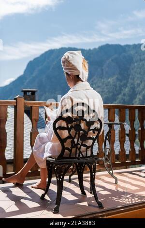 Frau, die einen entspannten Sommertag hatte und ein Buch auf einem Balkon mit Blick auf die Berge las. Allein Mädchen in einem ländlichen Rückzugsort und Spa Stockfoto