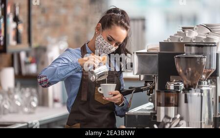 Kellnerin bereitet Capuccino in einem Café mit Schutzmaske. Stockfoto