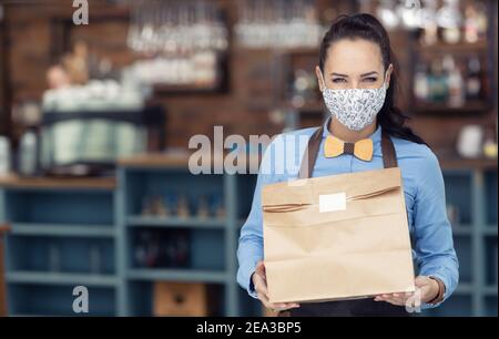 Gesichtsmaske trägt Restaurantmitarbeiter übergibt Takeaway Paket während Lockdown. Stockfoto