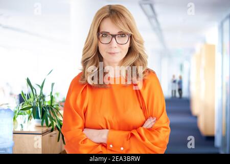 Porträtaufnahme einer Geschäftsführerin, die im Büro steht und die Kamera anschaut und lächelt. Stockfoto
