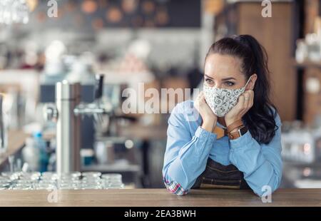 Kellnerin steht in einem Kaffeehaus mit nichts zu tun, trägt Schutzmaske, warten auf Kunden. Stockfoto